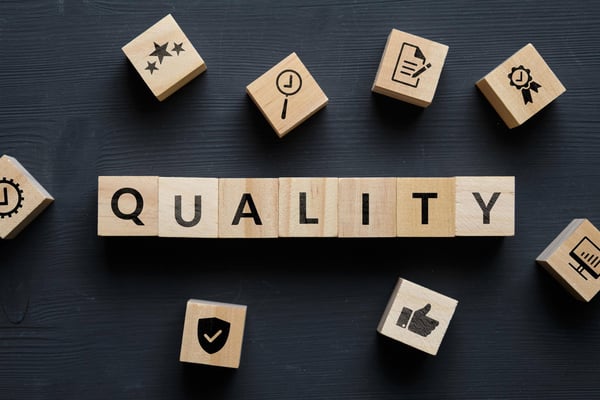 The word quality printed on wooden blocks with blocks with icons like thumbs up surrounding them