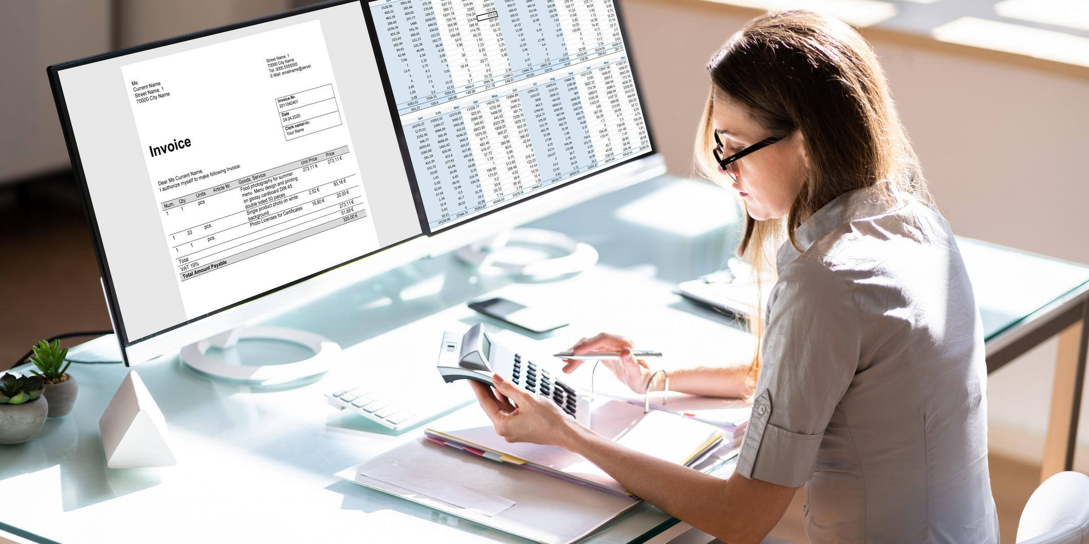 Businesswoman sitting at her desk viewing an invoice on one computer monitor and a spreadsheet on a second monitor
