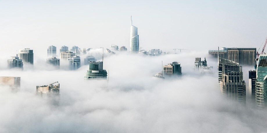 Illustration that shows a view of a cityscape set in the midst of clouds in soft focus 