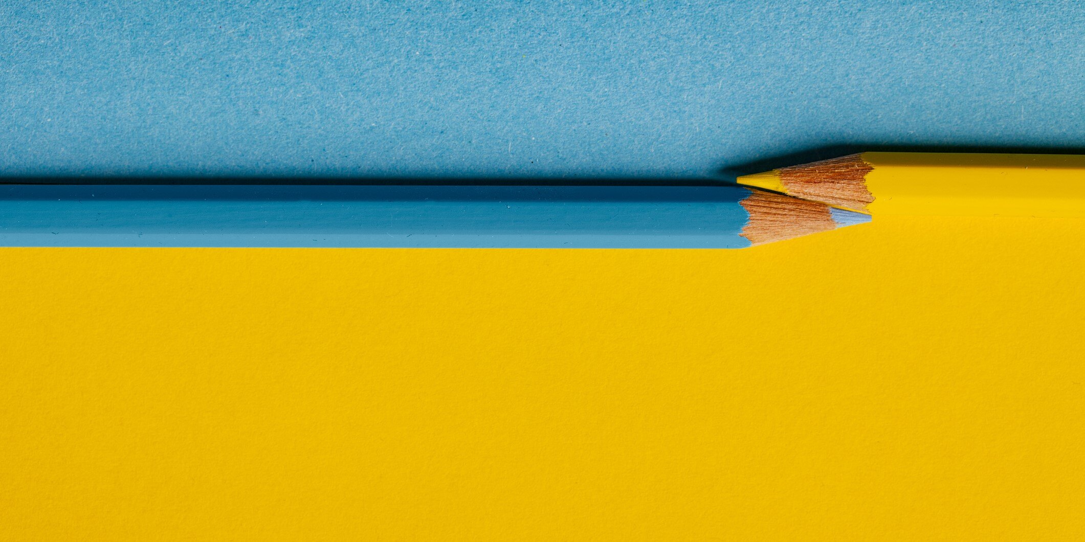 Photograph of a yellow and blue colered pencil on a background that is one-third blue and two-thirds yellow