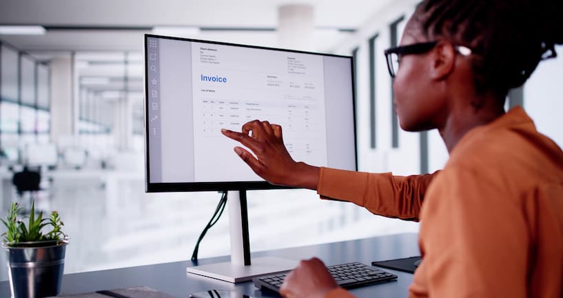 woman sitting in front of a monitor pointing on an invoice